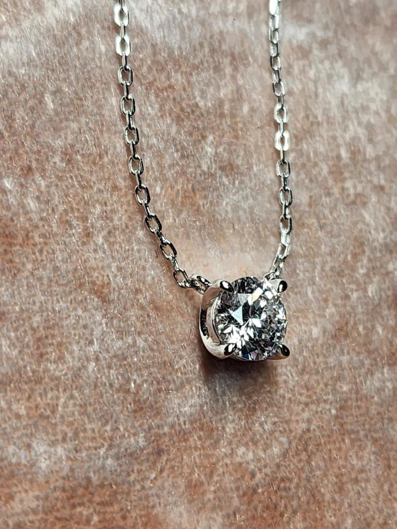 side view of One sterling silver round lab grown diamond necklace on a chain on a pink velvet background