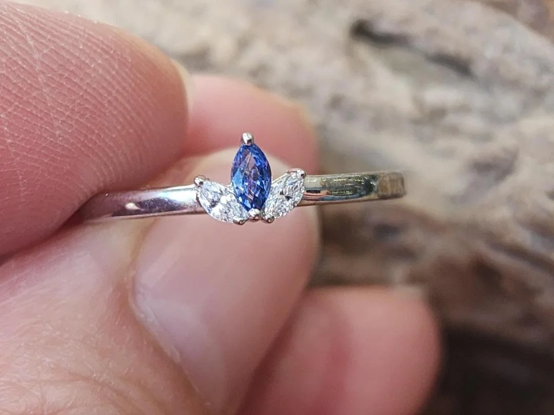 fingers holding Yogo sapphire and diamond ring with burlap background