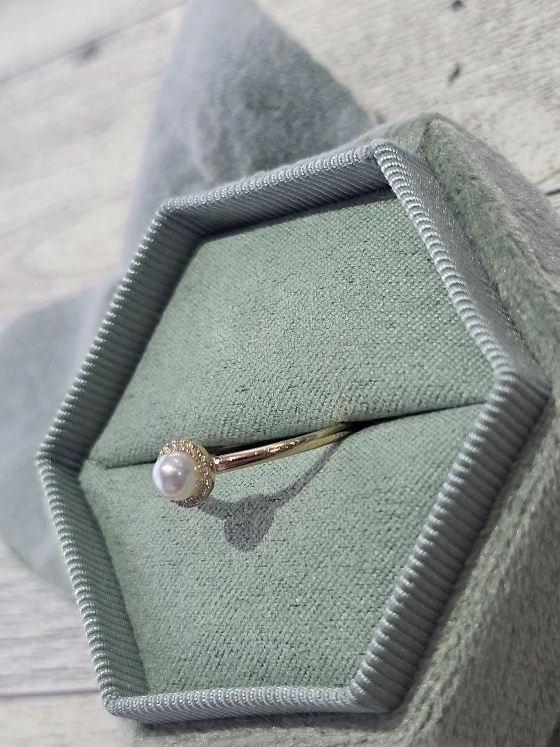 yellow gold ring with freshwater cultured pearl and halo of round diamonds in a green box with a wood back round