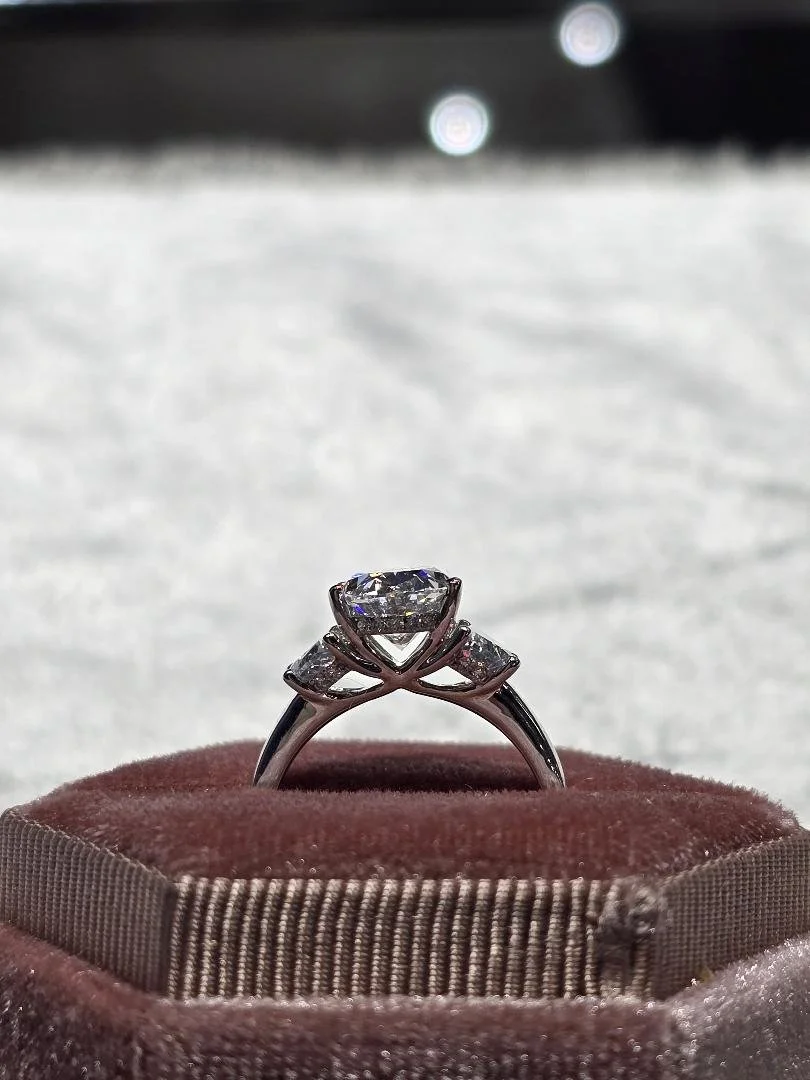 Side profile view of a white gold three stone styled lab grown diamond ring set in a pink velvet box on a grey velvet background