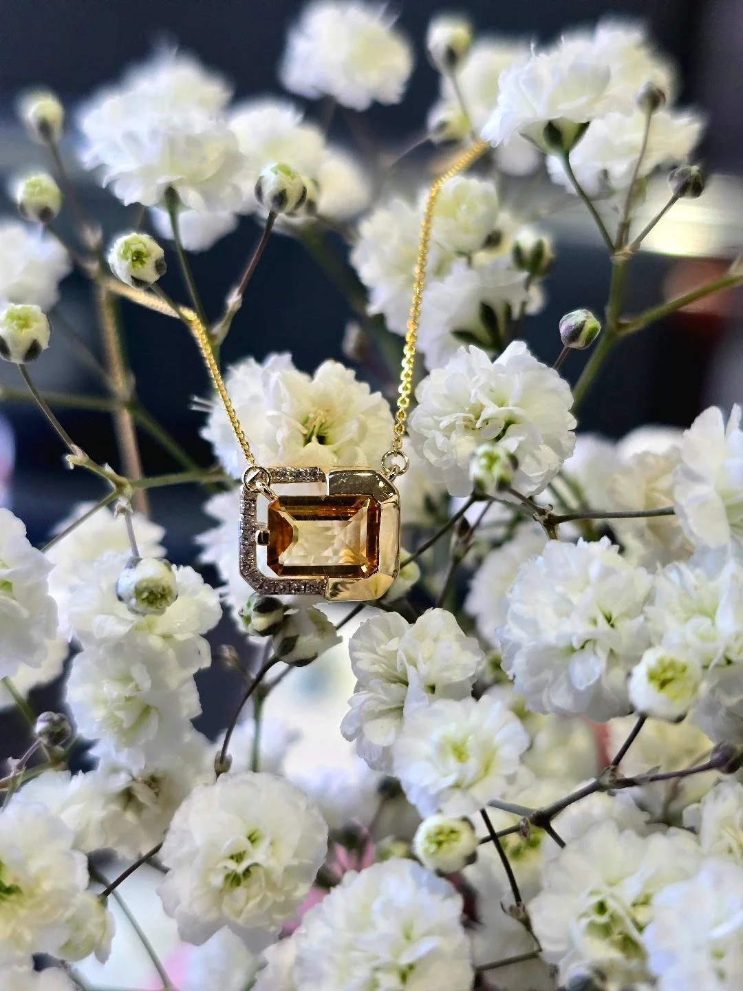Front view of yellow gold citrine pendant on a background of small white flowers
