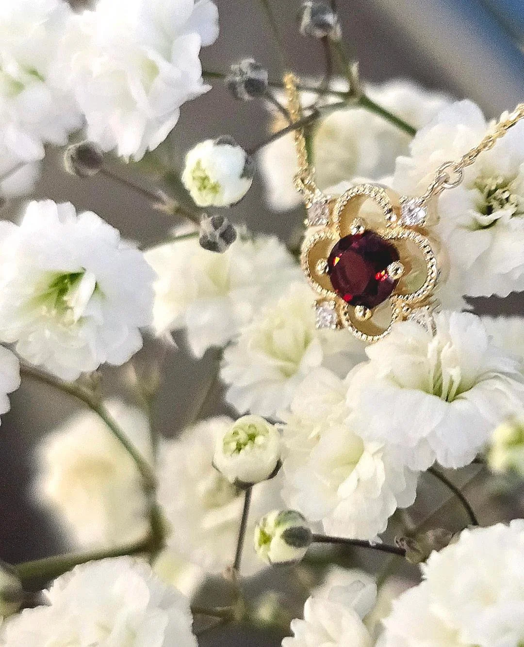 Side view of yellow gold garnet pendant on a small white flower background
