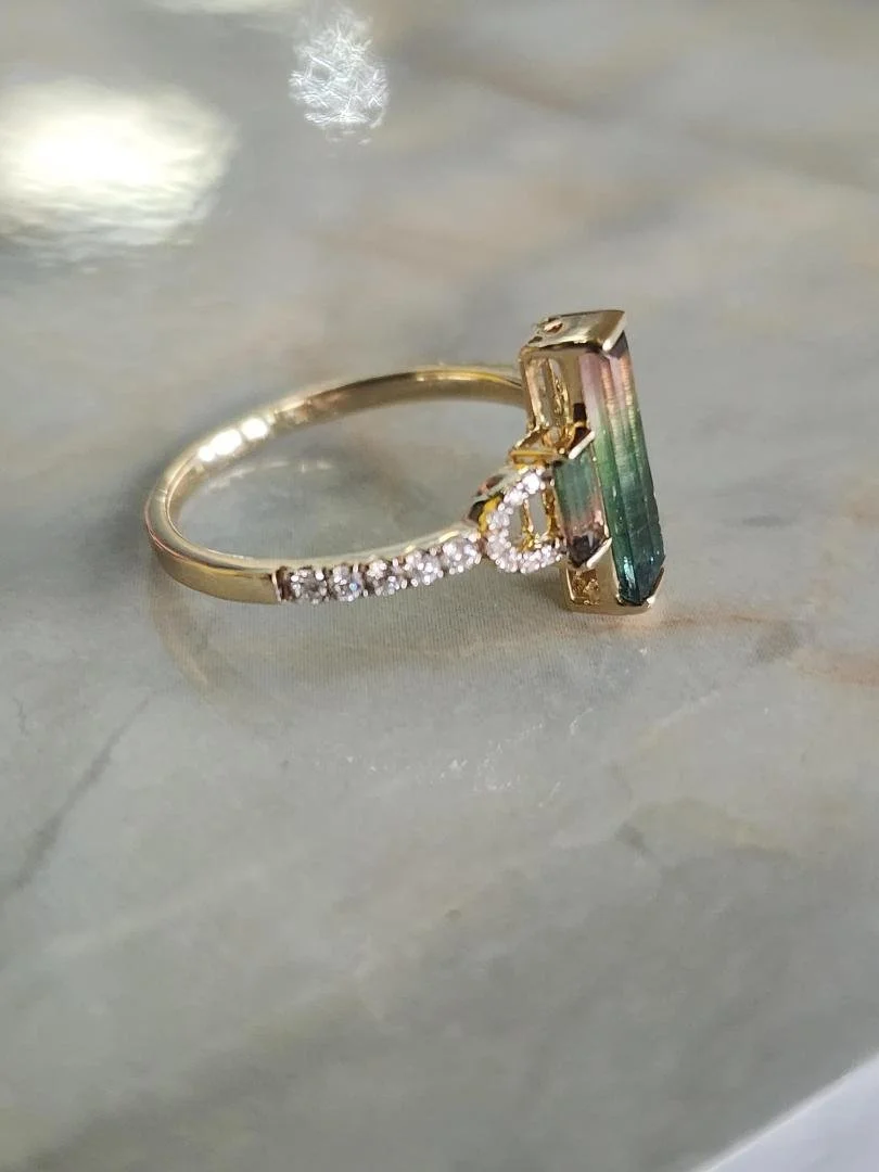 side view Yellow gold ring with 3 stone watermelon tourmaline and diamonds on a marble background