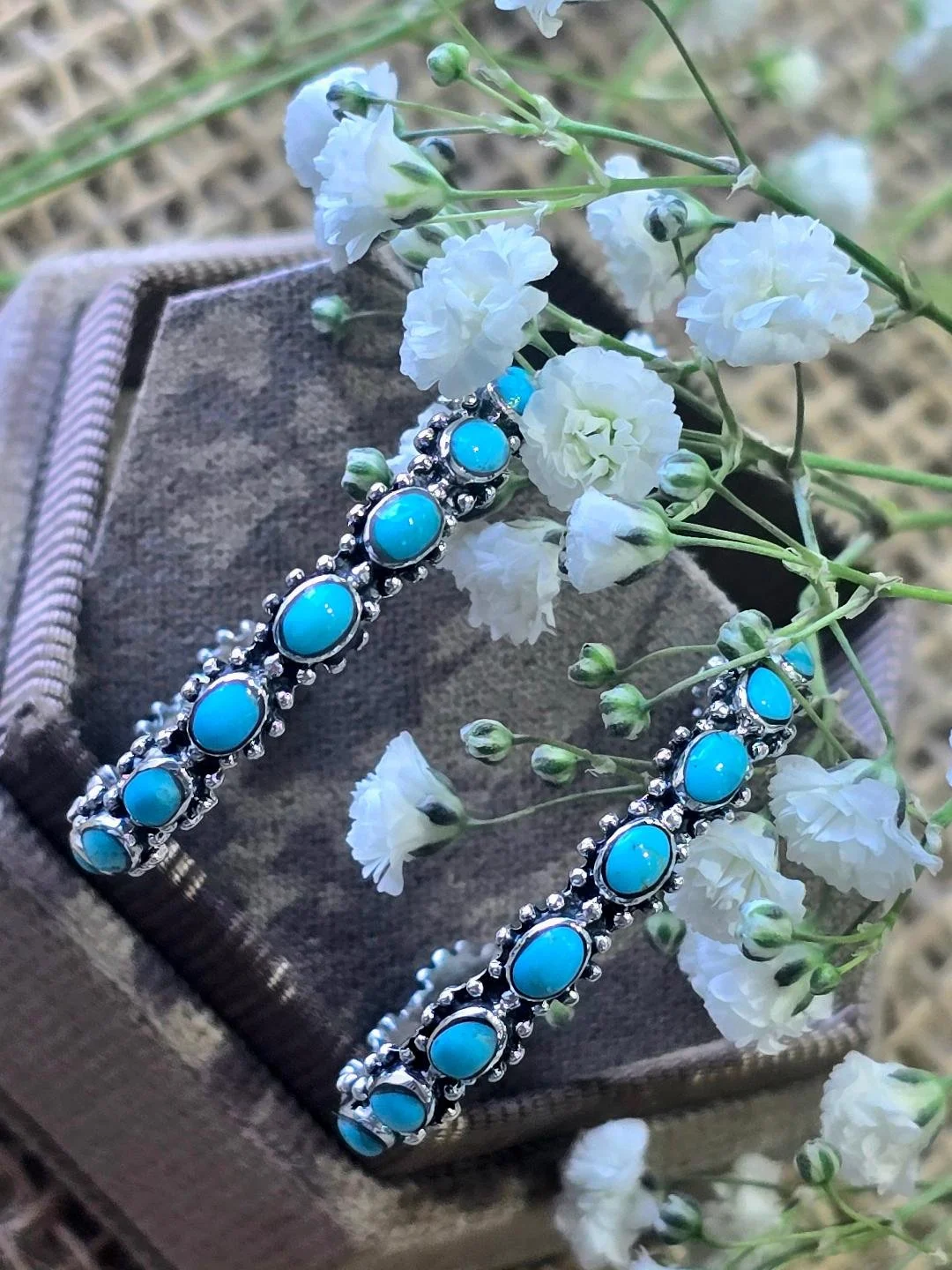 Angled view of oval turquoise hoops in brown box with white flowers