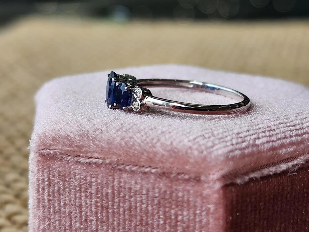 side view white gold 3 stone sapphire and diamond accent ring on a pink box with a brown background