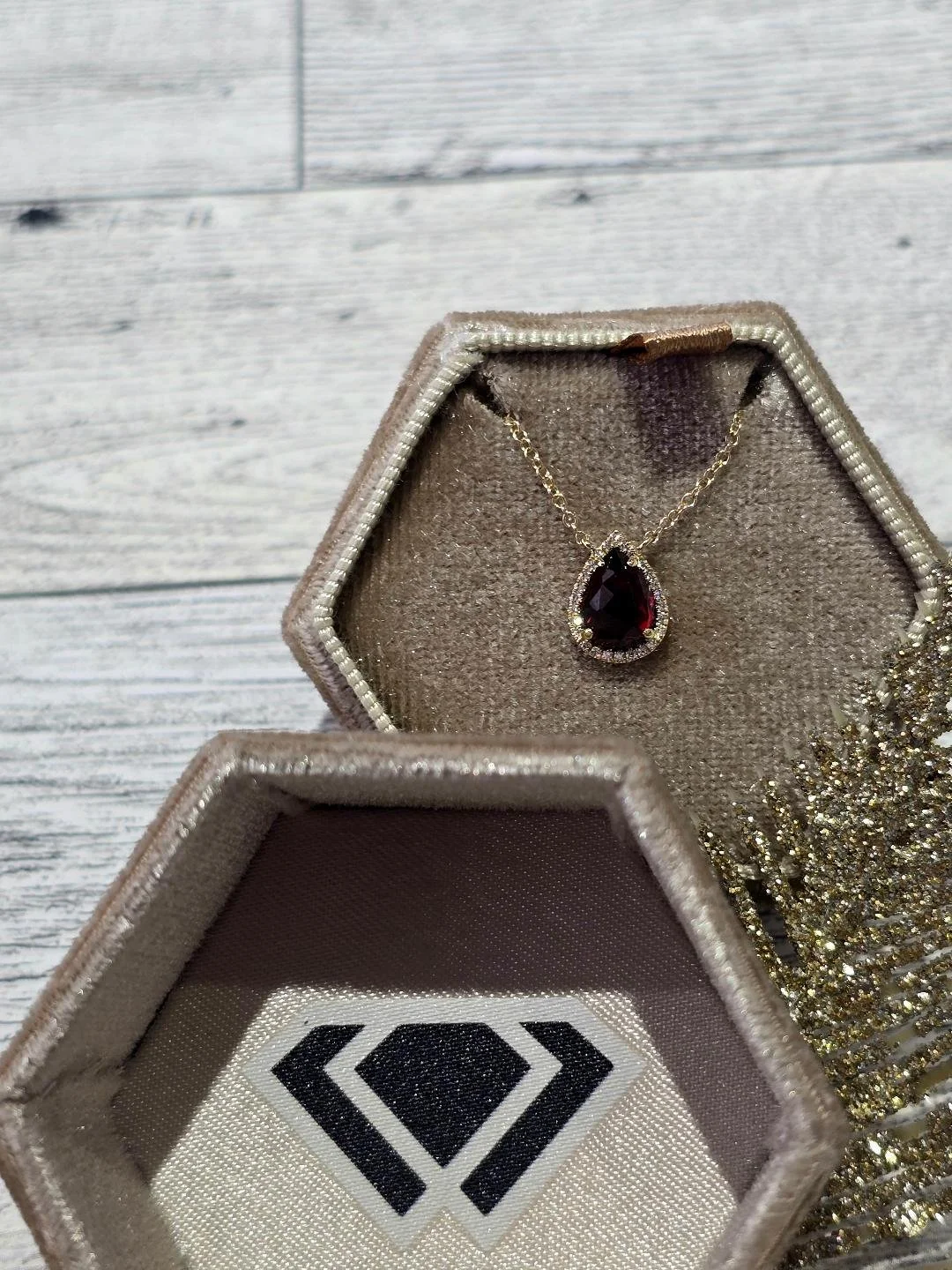 Front view of a yellow gold garnet and diamond stationary pendant in a brown box with a white wood background