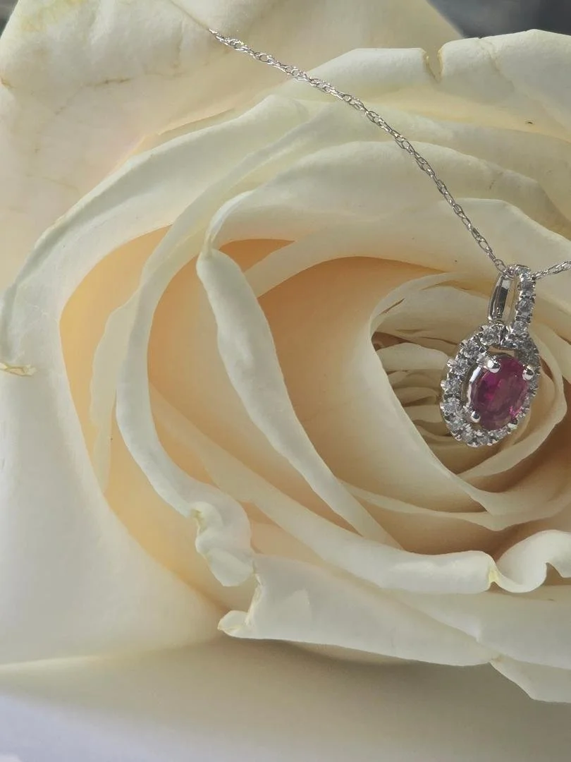 Side view of white gold oval pink tourmaline and diamond pendant on a white rose background