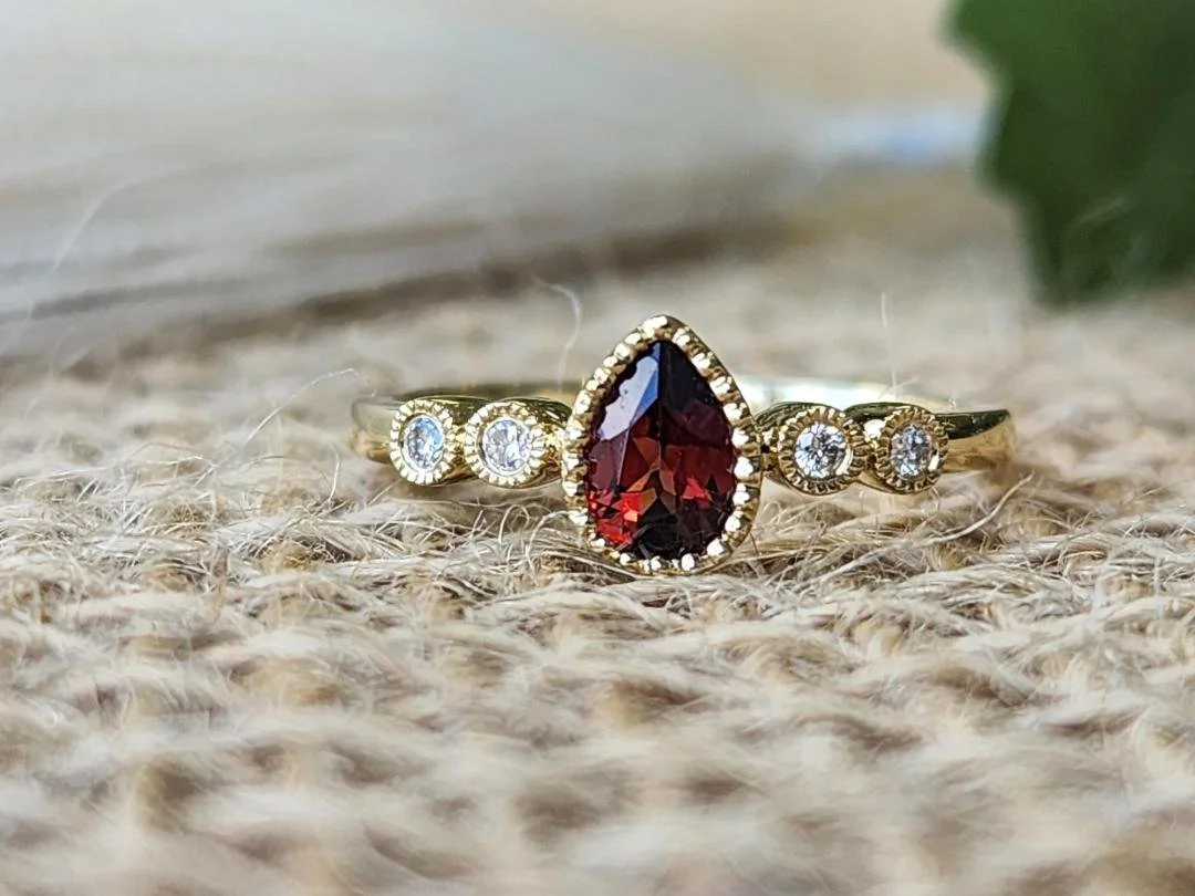 Pear shaped garnet ring in yellow gold with burlap and objects in background