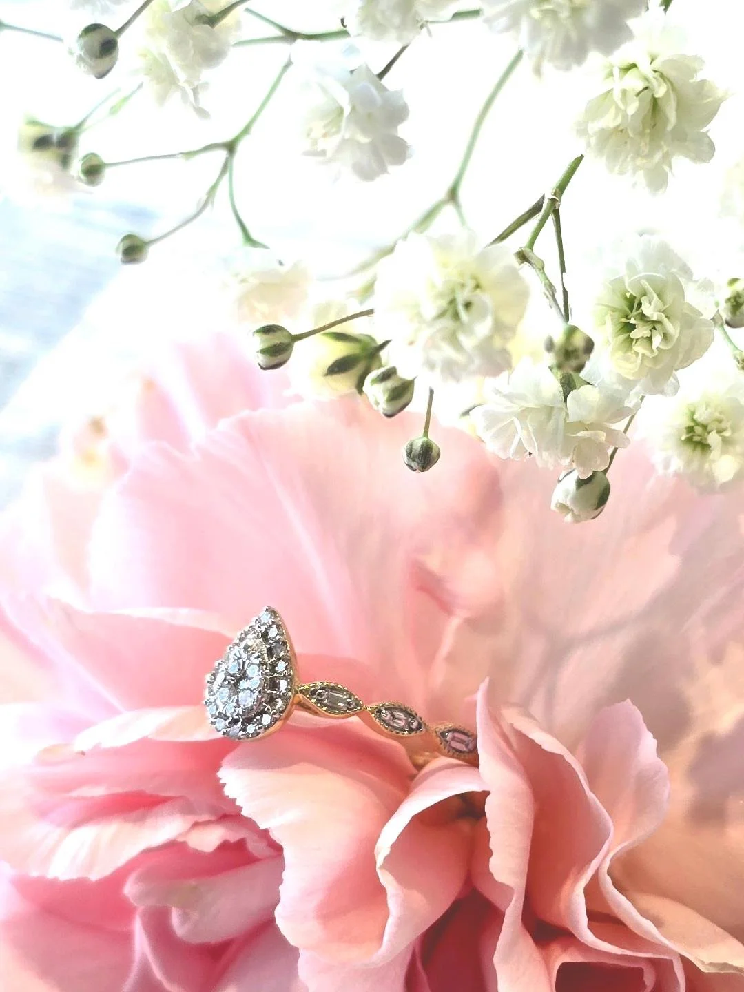 Side view of yellow gold pear shaped ring set in a pink carnation with white flower