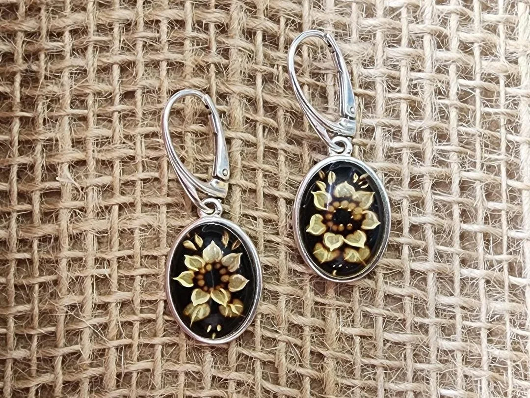 Pair of sterling silver amber earrings with a carved sunflower on burlap