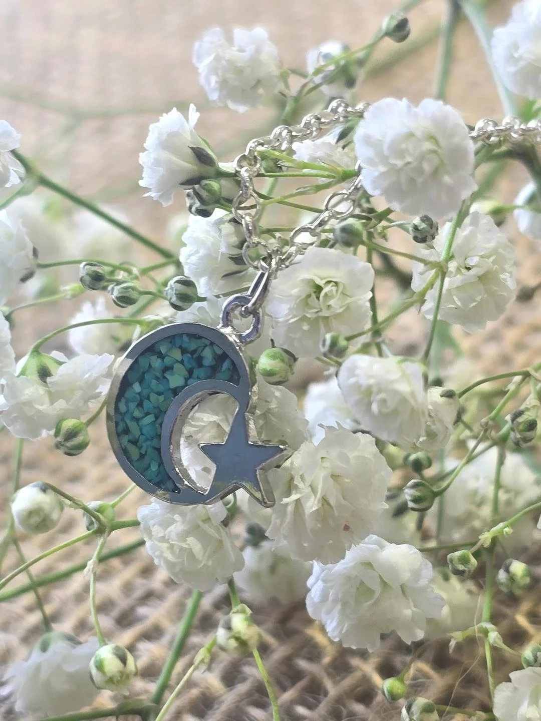 Side view of silver crescent moon & star pendant of white flower background