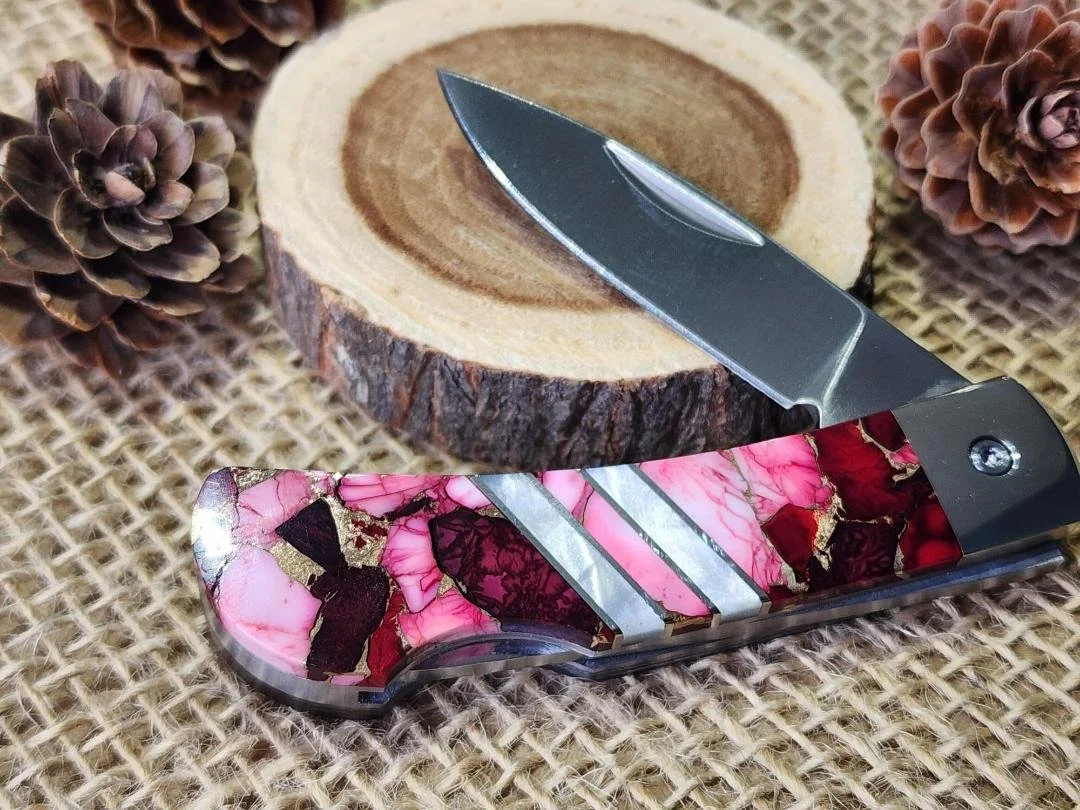 open 3" knife the "red dahlia" with pink to red inlay and copper veining.  Then two mother of pearl stripes in the center on wood display with pinecones and burlap in background