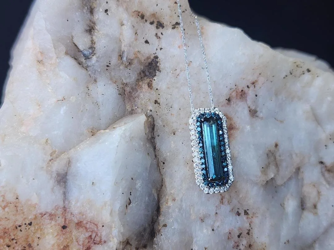 bi colored emerald cut tourmaline blue to green with a double halo of diamonds on a rock