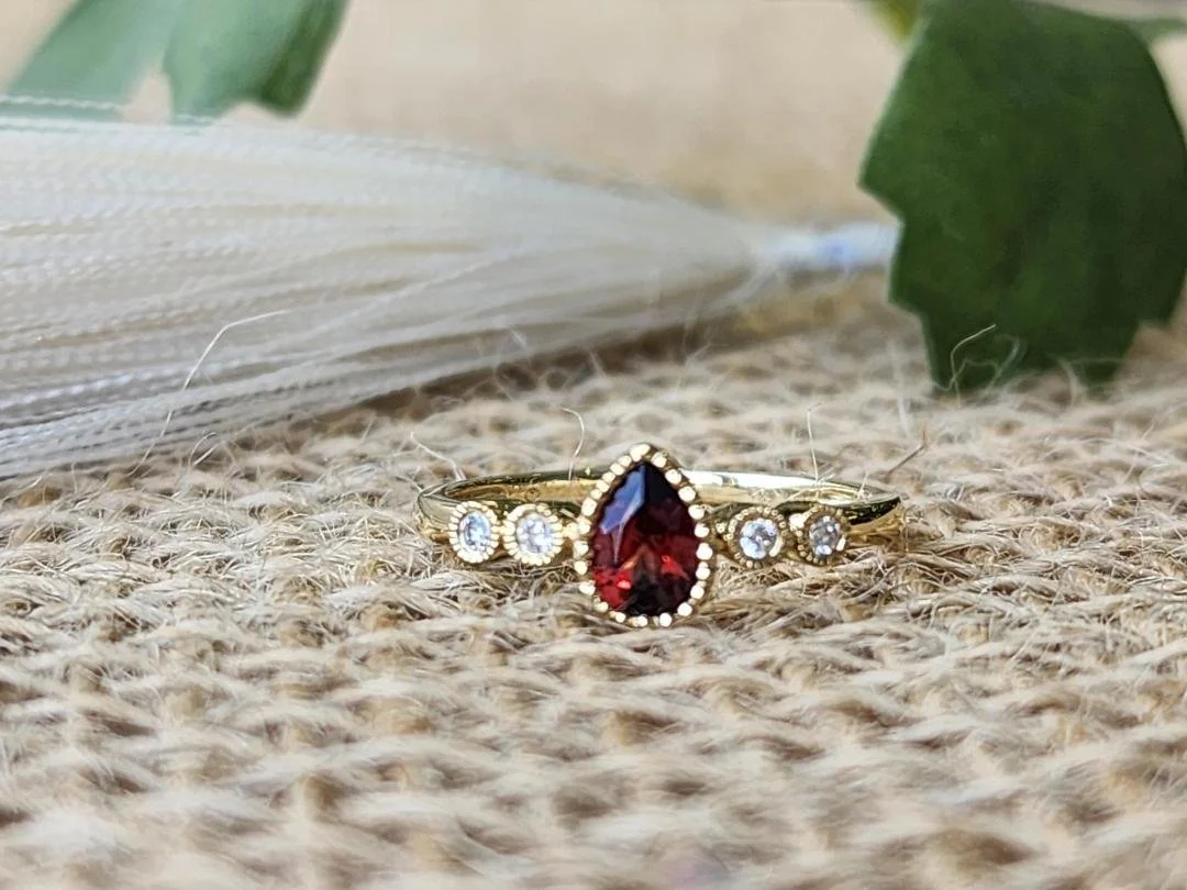 Pear shaped garnet ring in yellow gold with burlap and objects in background