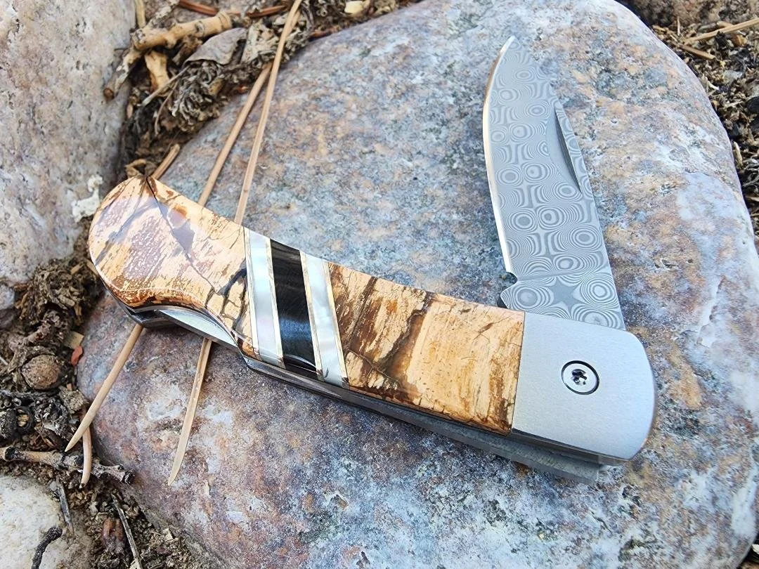 Damascus folding pocket knife on rock with mammoth handle and raindrop Damascus blade