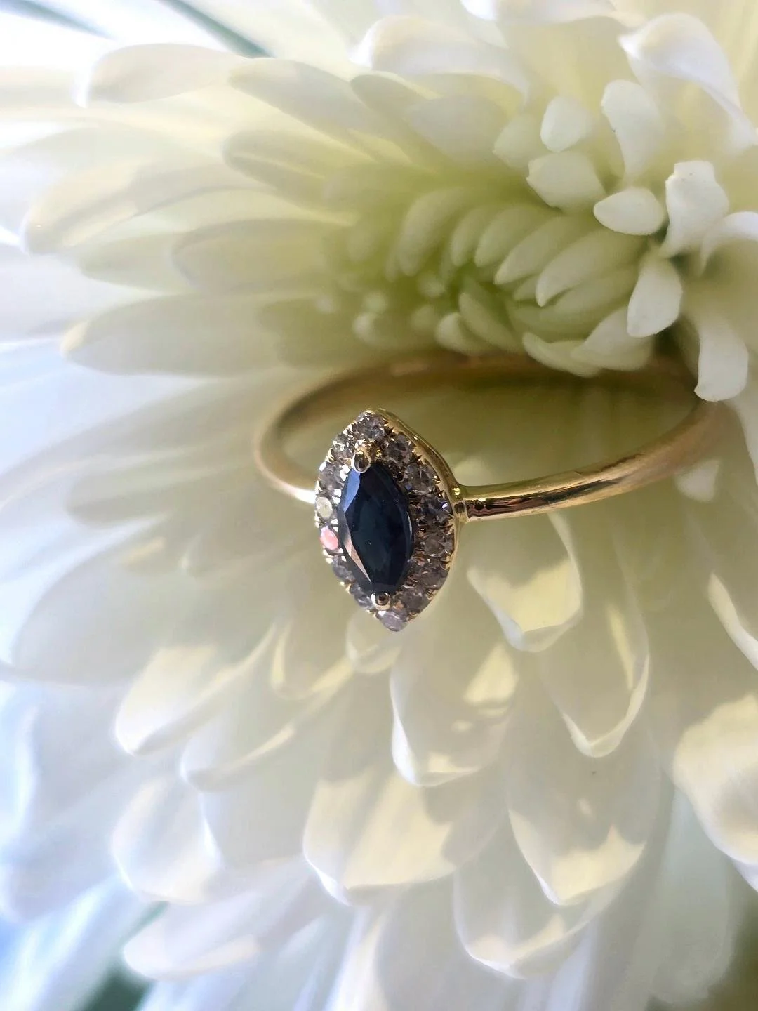 Side view of a yellow gold marquise sapphire ring with a diamond halo. The background is a white flower