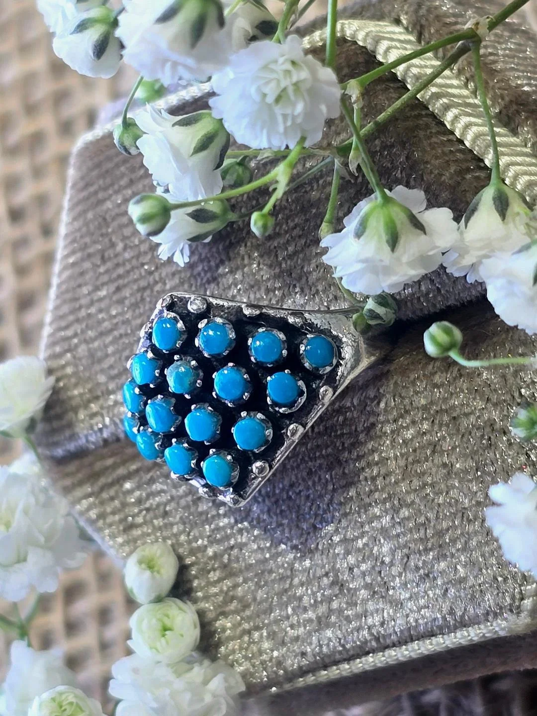 Side view of silver turquoise ring in a brown box with small white flowers set on top of the box