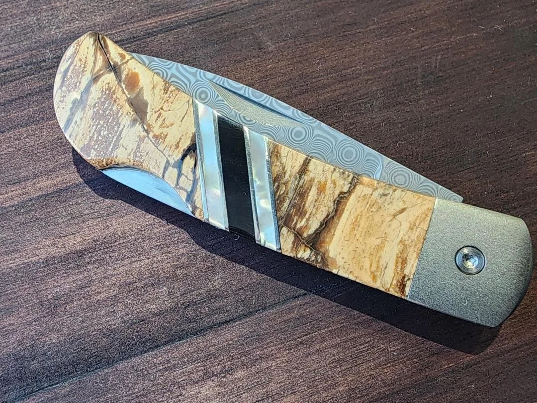 Closed Damascus folding pocketknife with mammoth handle and raindrop Damascus blade with wooden background
