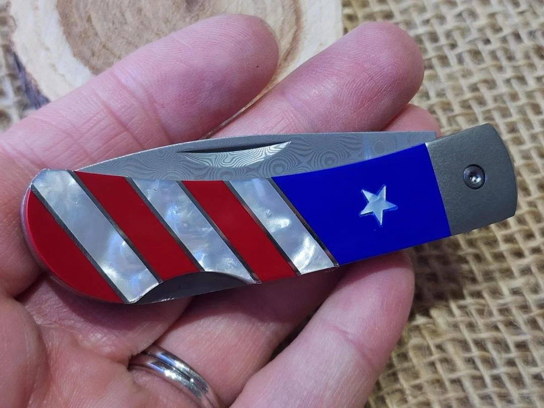 hand holding patriotic 3" knife with burlap and wood background
