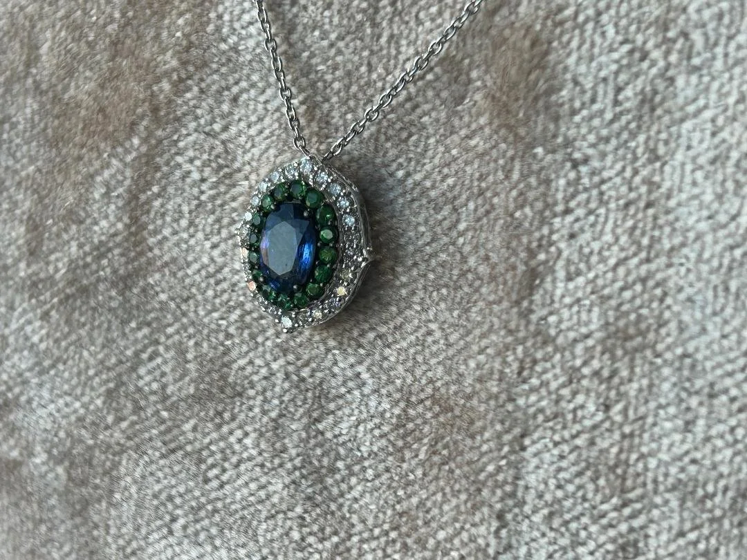 Blue sapphire with green tsavorite garnet, and diamond halo on pinkish grey fabric