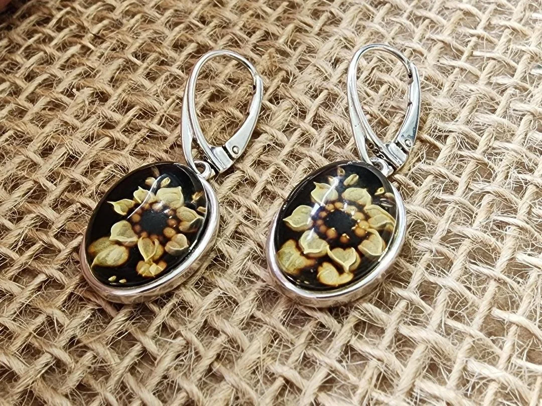 Pair of sterling silver amber earrings with a carved sunflower on burlap