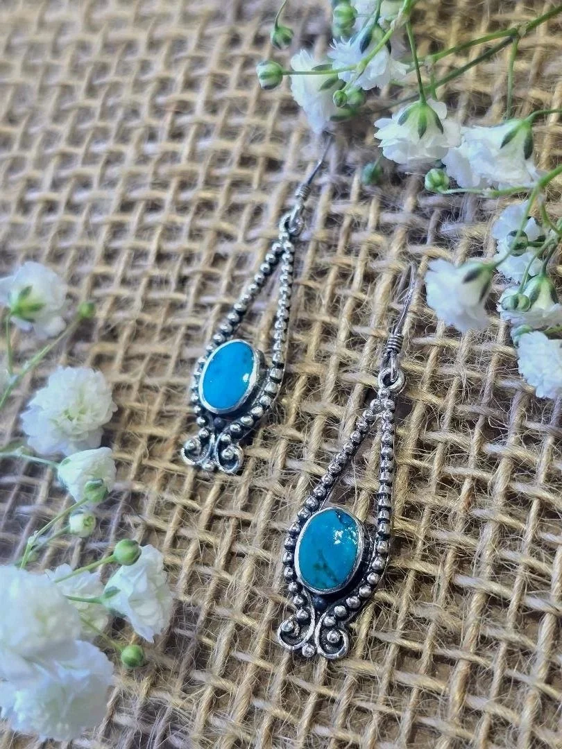 Side view of silver turquoise dangle earrings on a burlap background with white flowers on the corners
