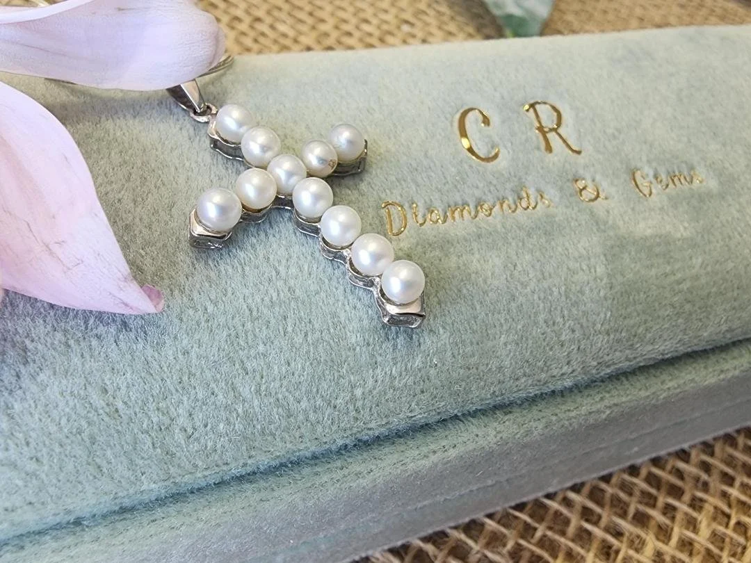 side view of sterling silver pearl cross on a blue green box with a flower and burlap in background