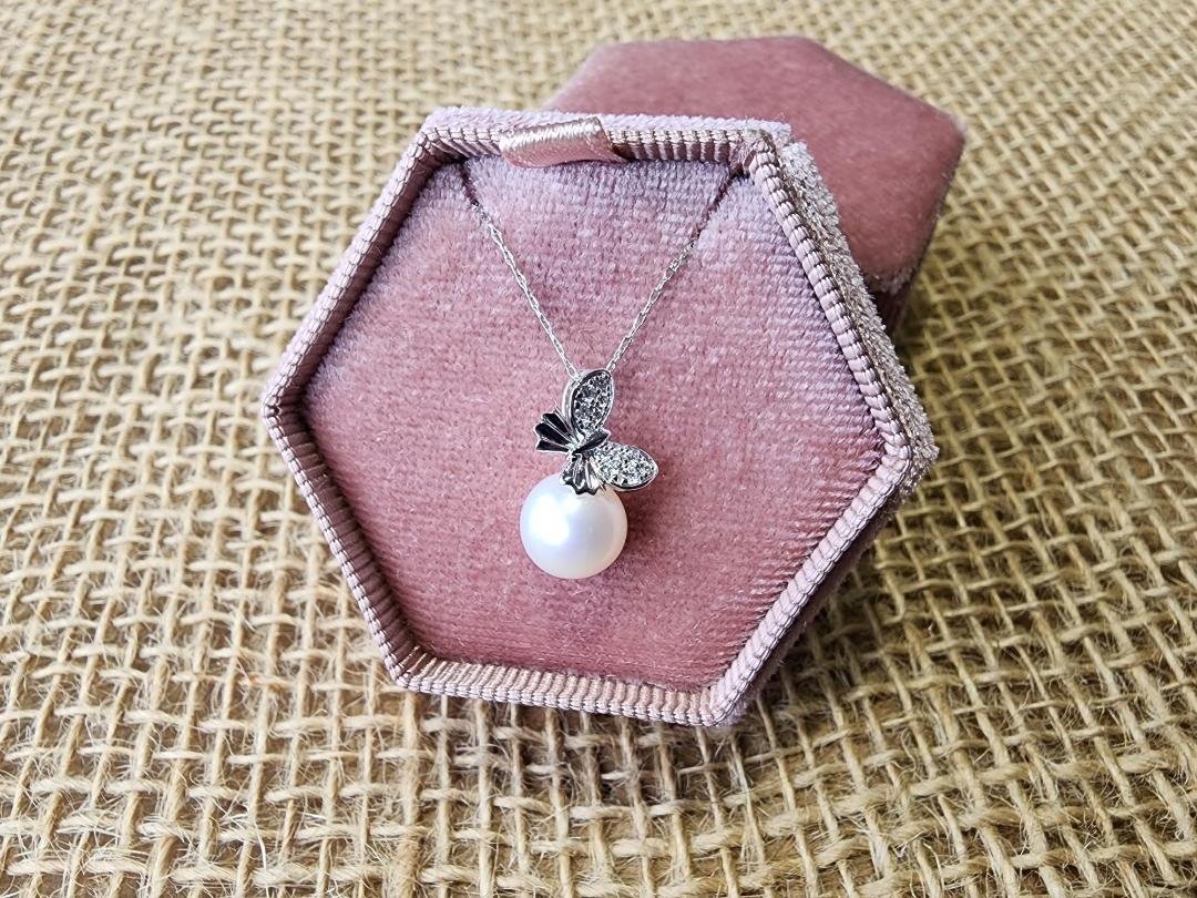 White gold diamond and pearl necklace with butterfly shape on pendant in a pink jewelry box on burlap