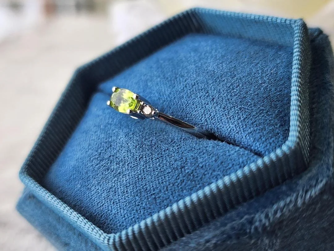 white gold peridot and diamond ring in a blue ring box with a grey background
