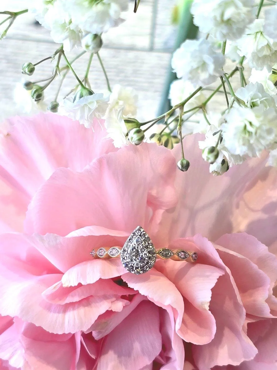 Front view of yellow gold pear shaped ring set in a pink carnation with white flower