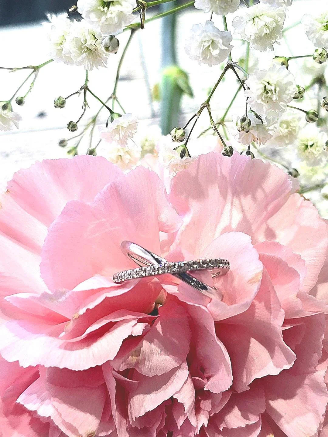 Front view of white gold crisscross ring set in a pink carnation with small white flowers at the top