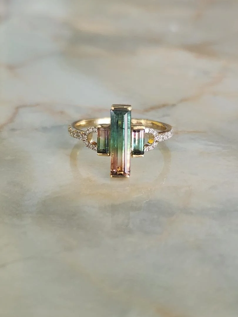 Yellow gold ring with 3 stone watermelon tourmaline and diamonds on a marble background