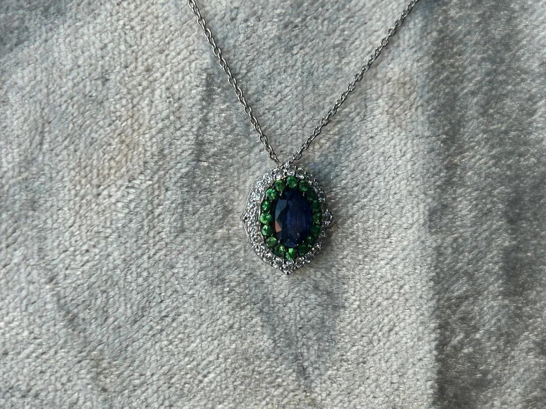 Blue sapphire with green tsavorite garnet, and diamond halo on pinkish grey fabric