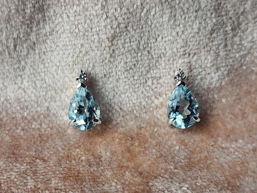 Pear shaped light blue aquamarine with diamond accent stud earrings on pink velvet background