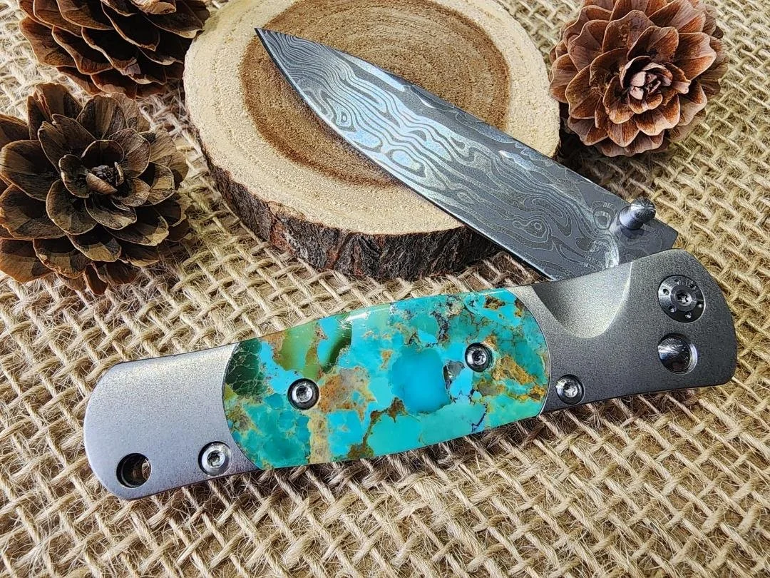 open One 3.5" damascus knife with a turquoise inlay on burlap with a wood slice and pinecones in background