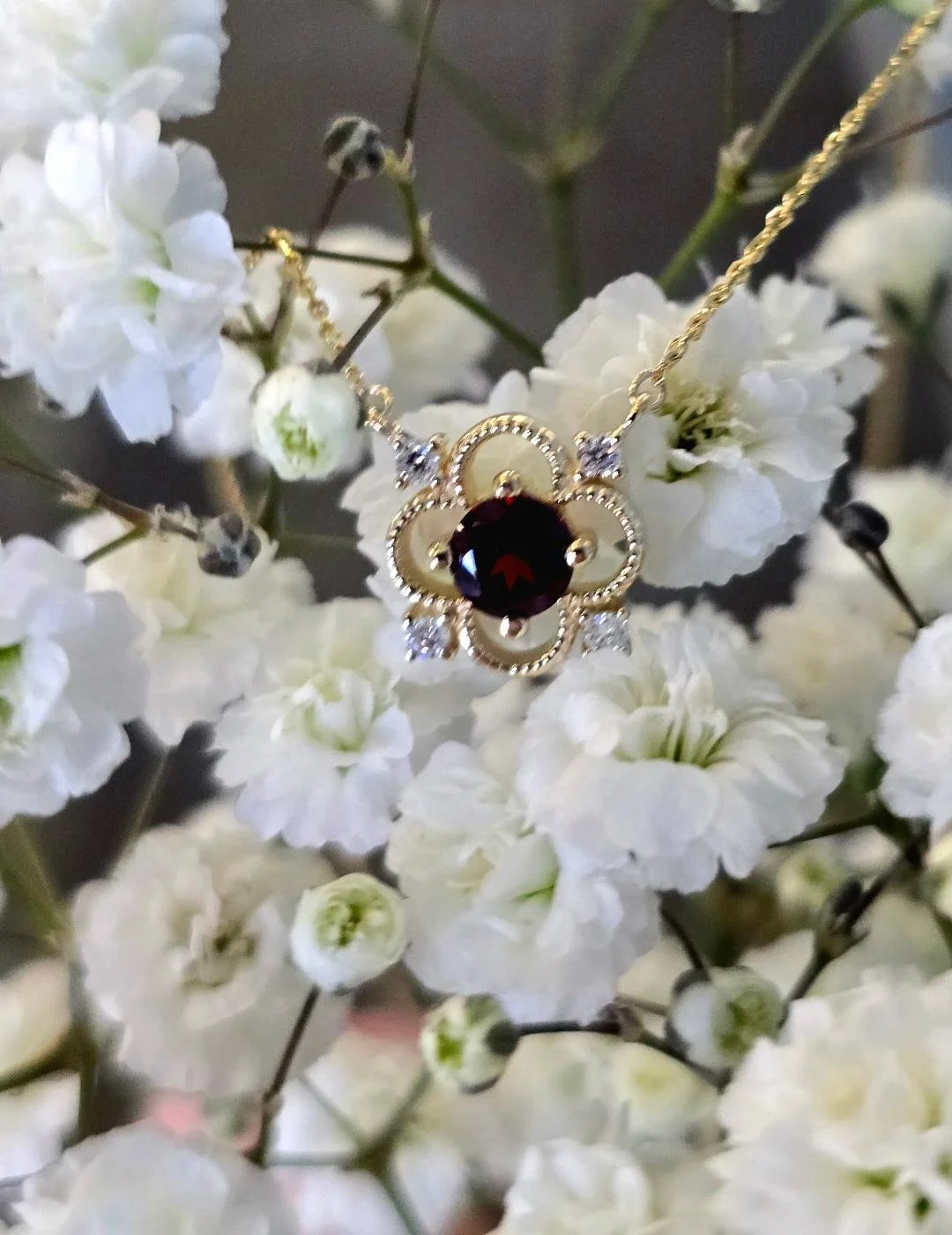 Front view of yellow gold garnet pendant on a small white flower background