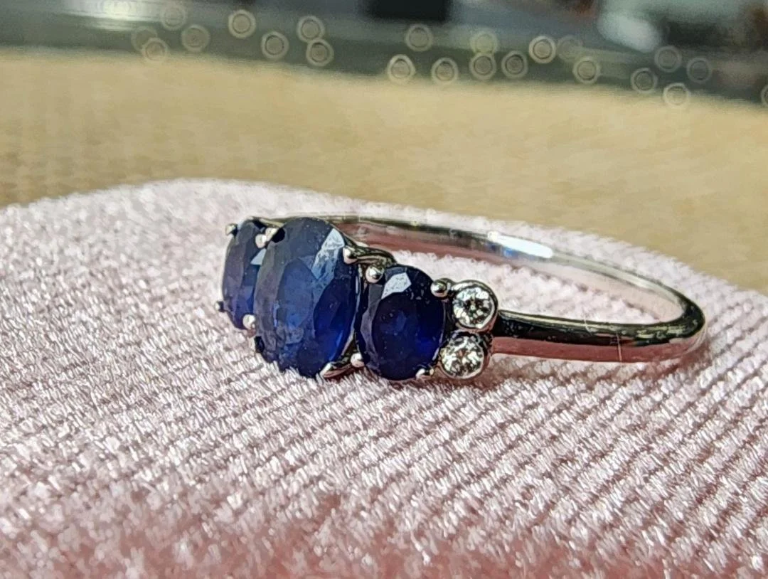 white gold 3 stone sapphire and diamond accent ring on a pink box with a brown background