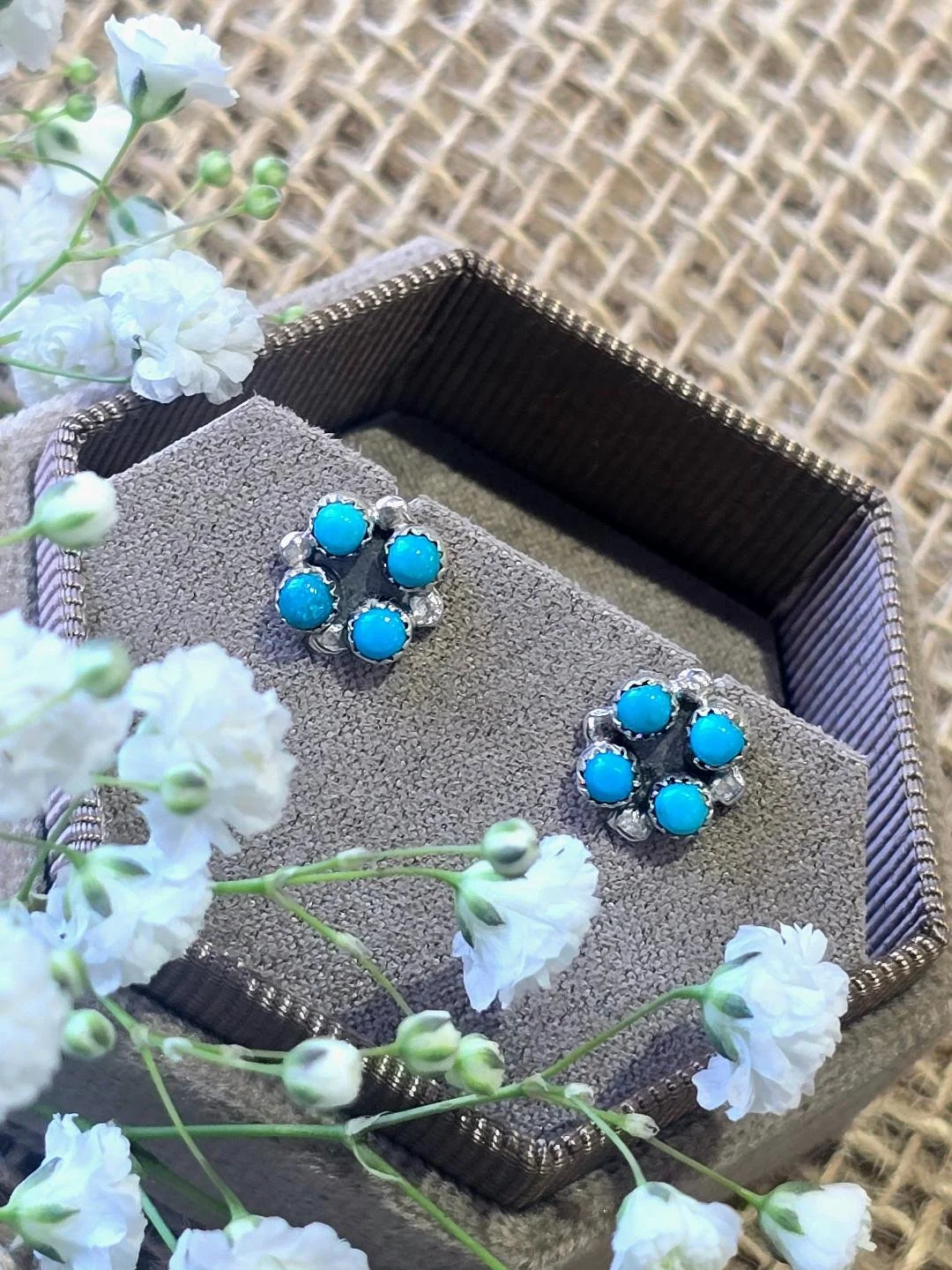 Angled view of silver turquoise studs in a brown bracelet with small white flower set on top
