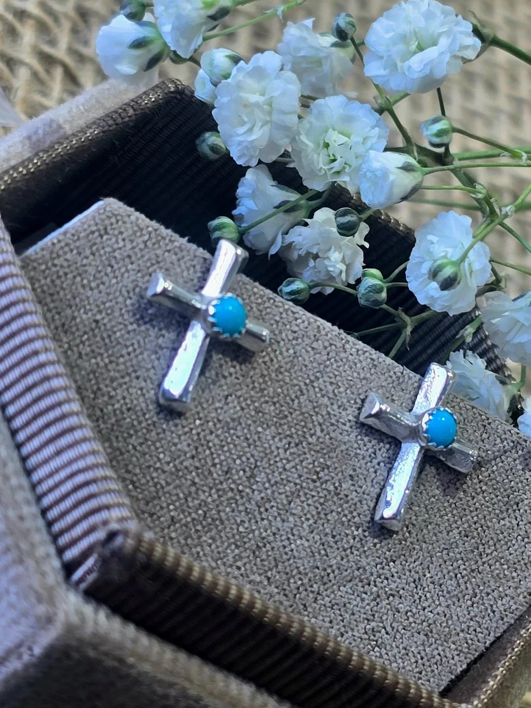 Side view of silver polished cross studs in a brown box with small white flowers set on top