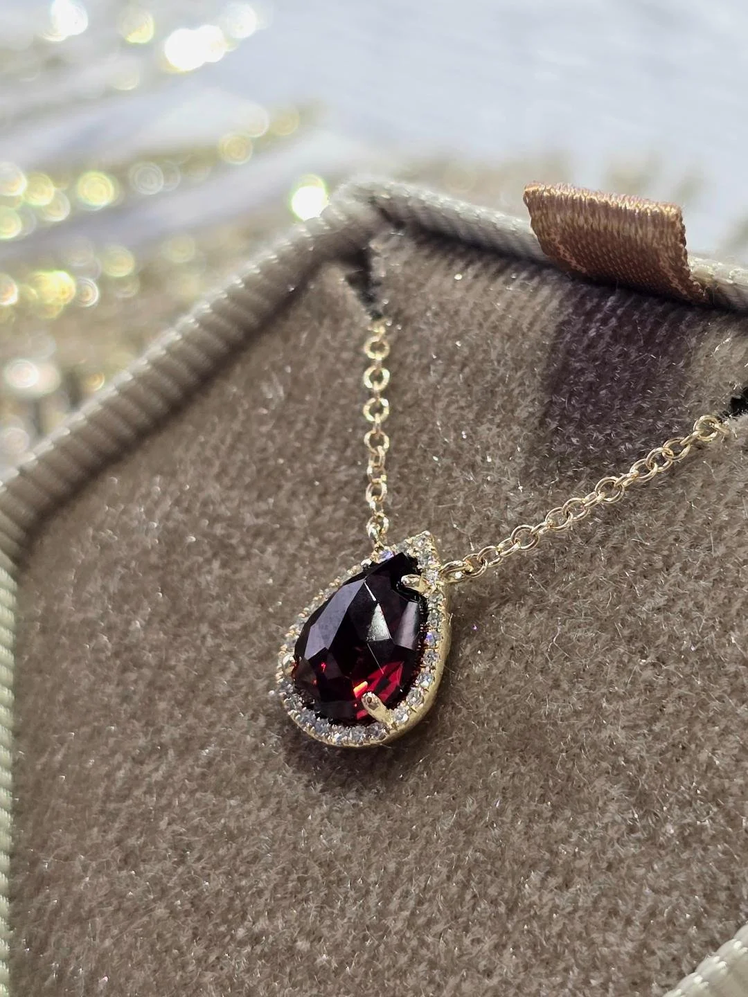 Side view of a yellow gold garnet and diamond stationary pendant in a brown box with a white wood background