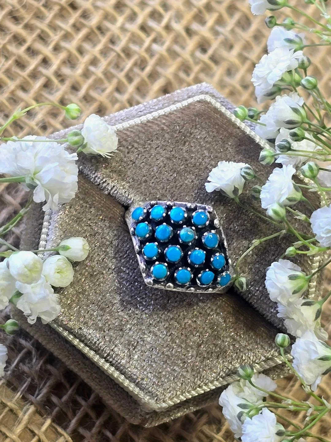 Side view of silver turquoise ring in a brown box with small white flowers set on top of the box