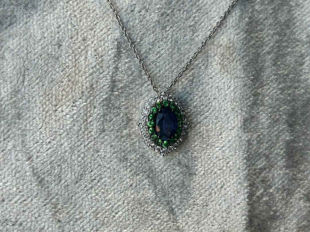 Blue sapphire with green tsavorite garnet, and diamond halo on pinkish grey fabric