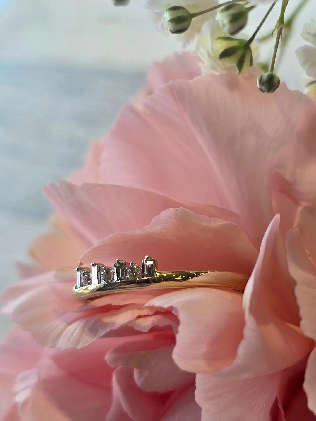 Side view of yellow gold band set in a pink carnation with small white flower at the top