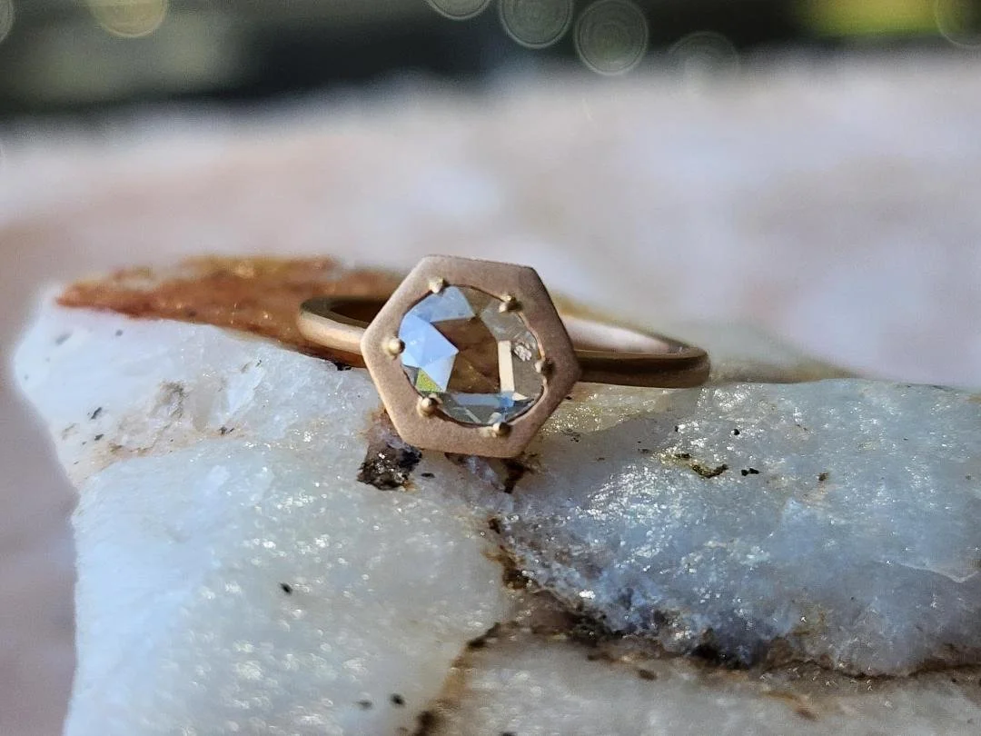 Brushed Rose gold diamond ring with rose cut diamond  resting on white quartz with pink and black background