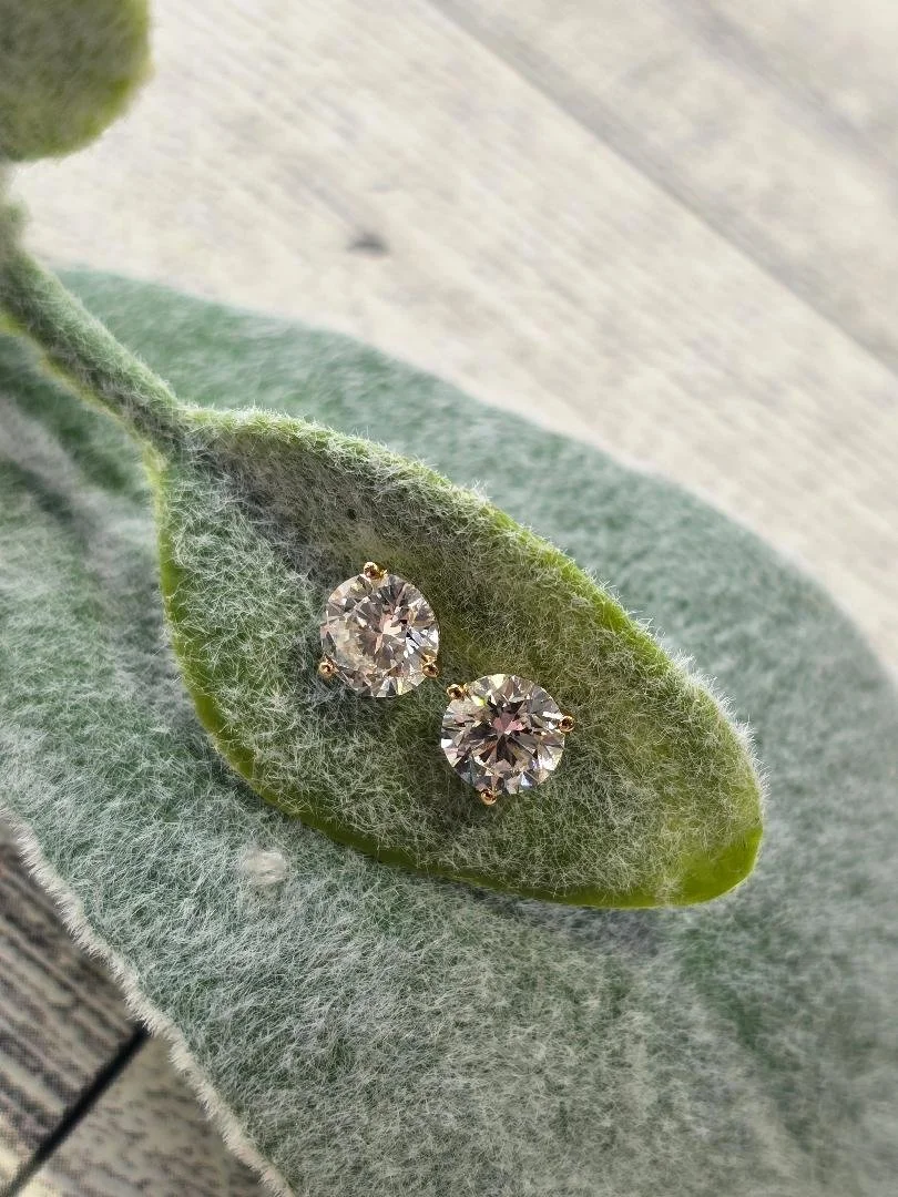 Front angled view of lab grown diamond studs set in a leaf on a white wooden background