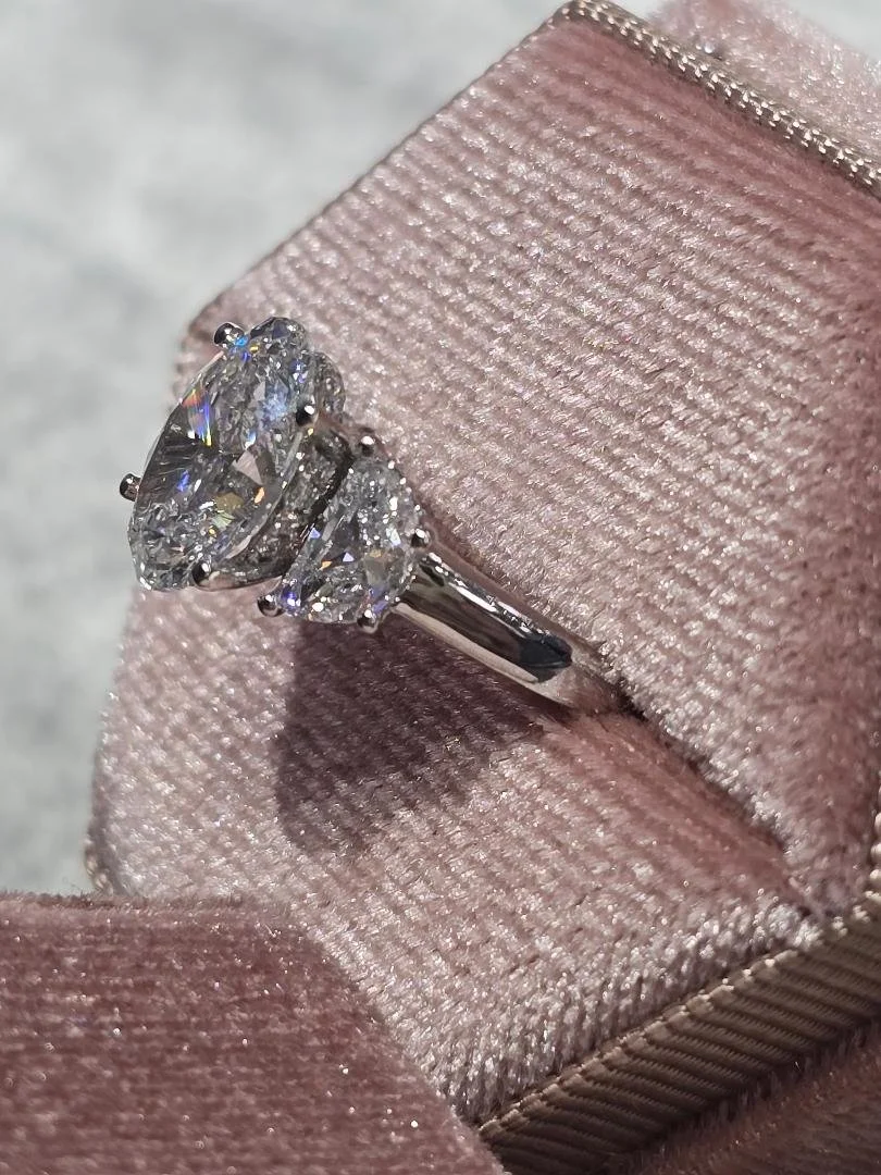 Side view of a white gold three stone styled lab grown diamond ring set in a pink velvet box on a grey velvet background