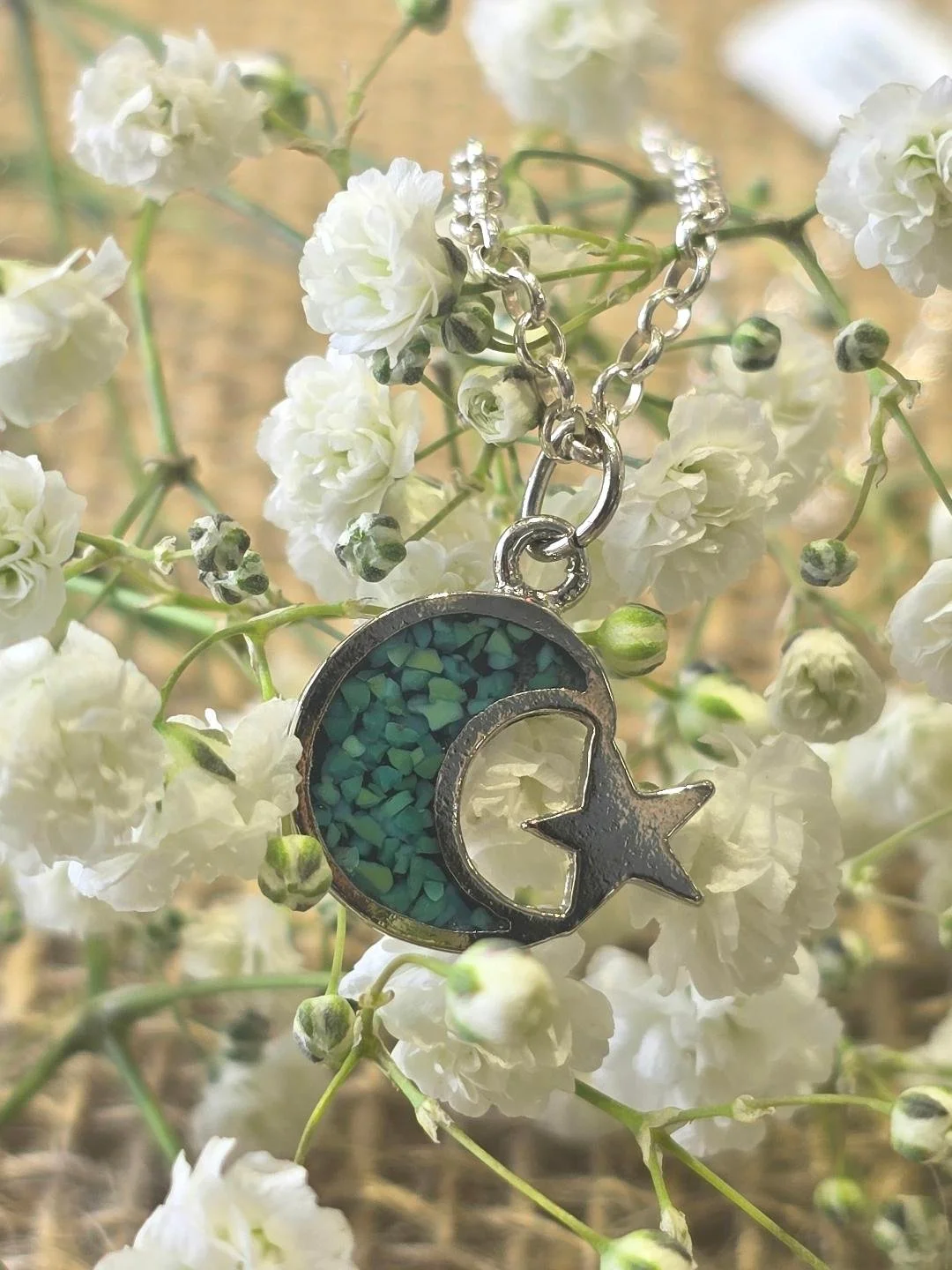 Front view of silver crescent moon & star pendant of white flower background