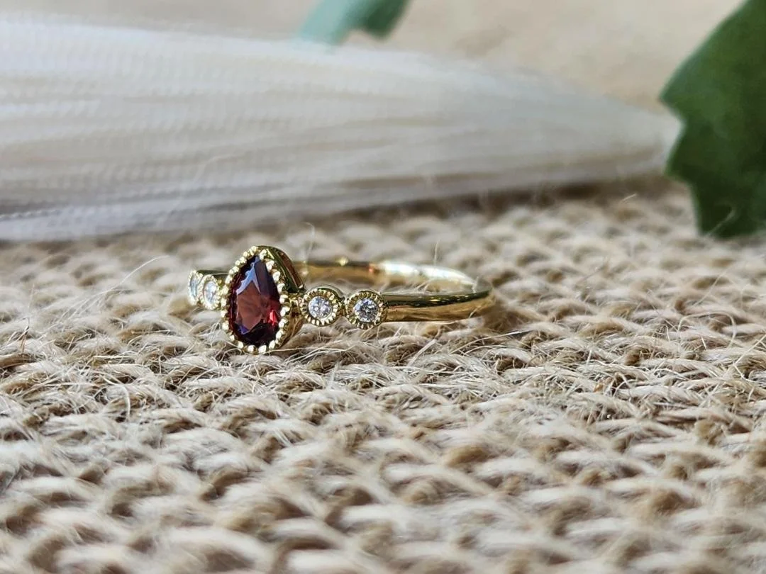 Pear shaped garnet ring in yellow gold with burlap and objects in background