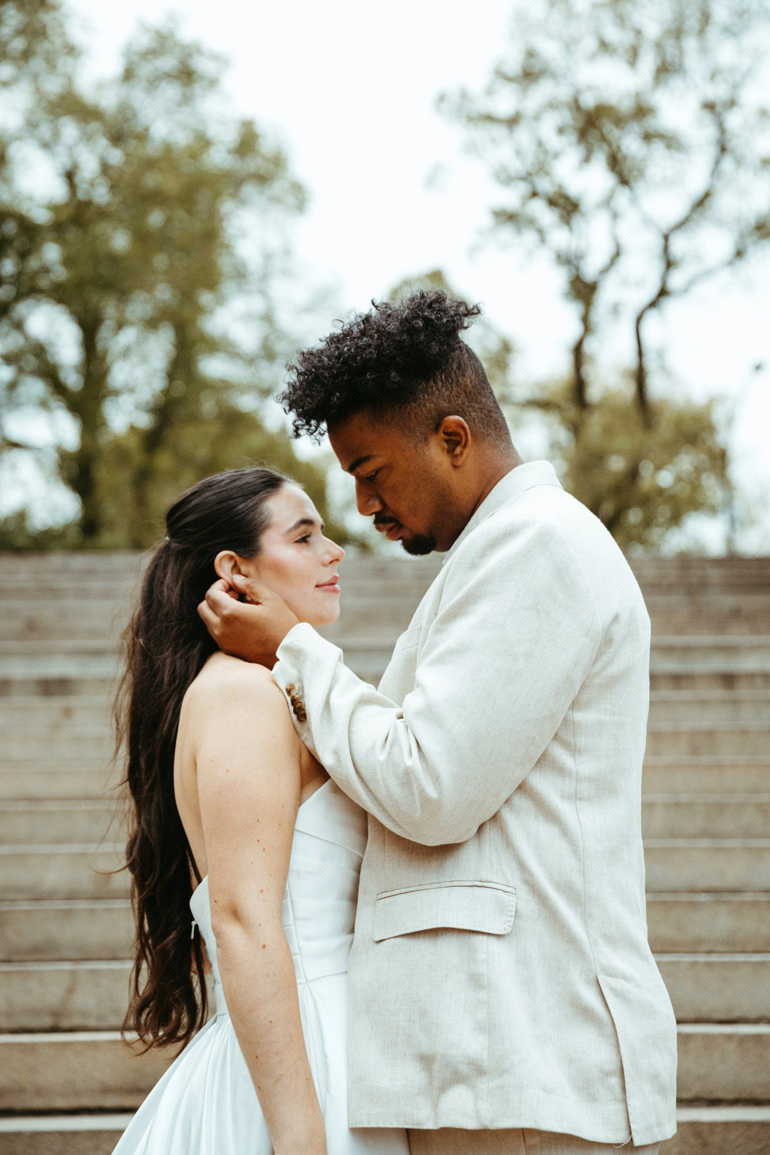 A couple in wedding attire sharing an intimate moment on outdoor staircase with trees in the background