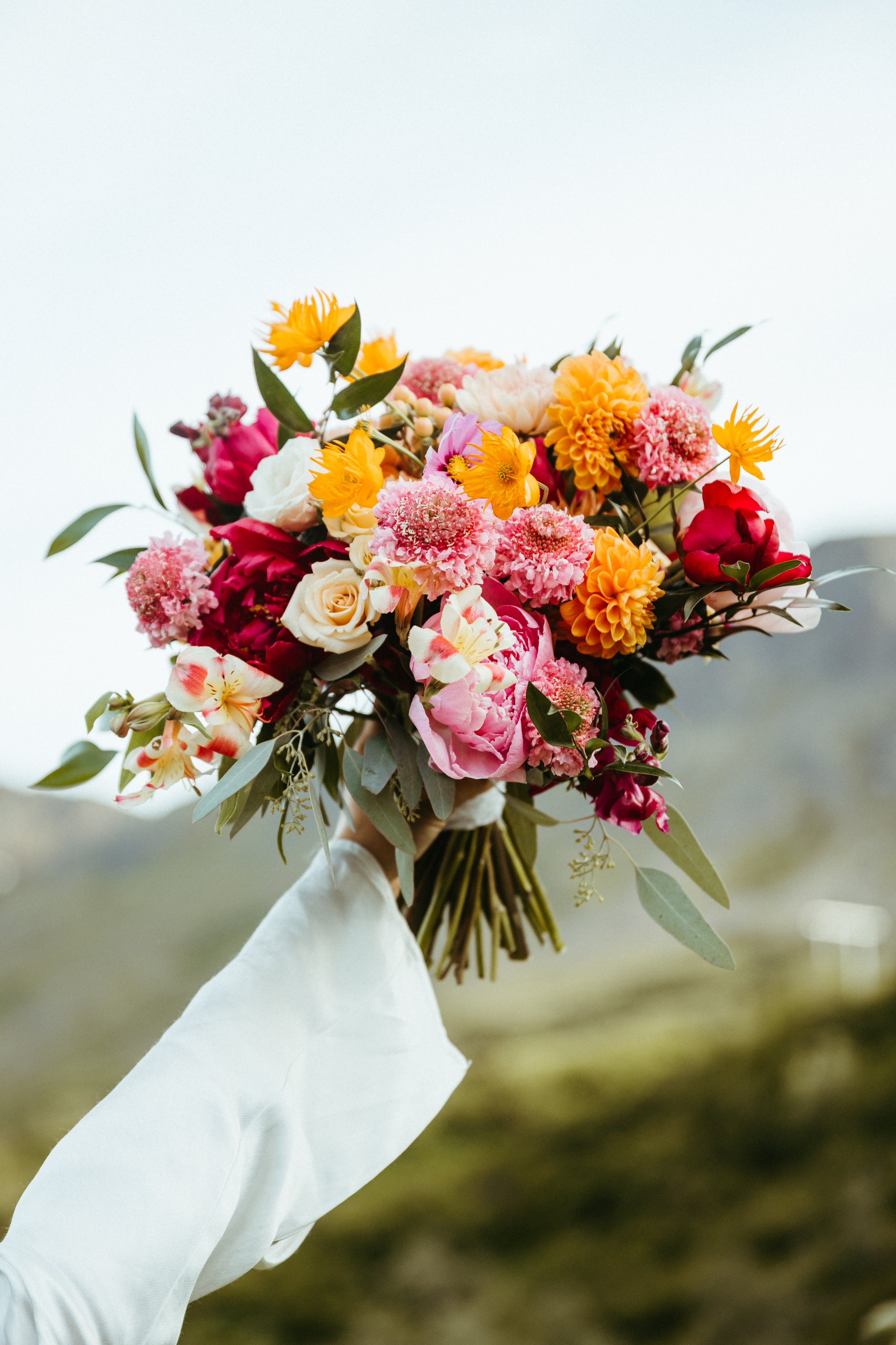 Person holding a colorful bouquet of various flowers outdoors.